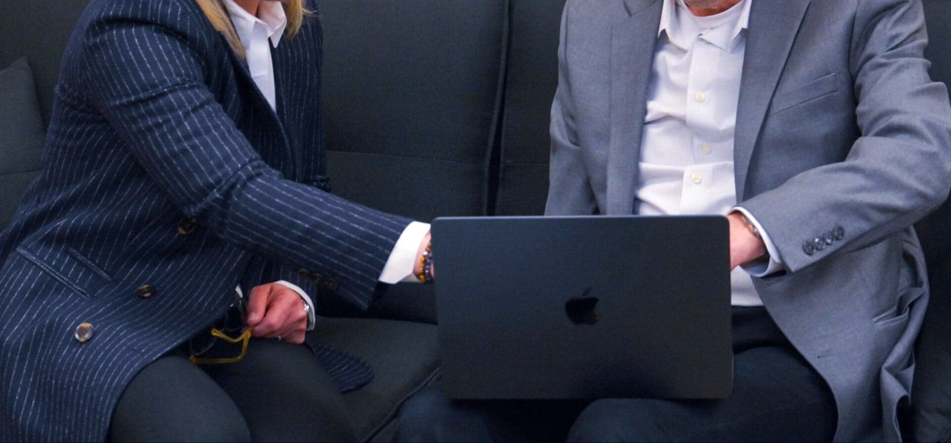 Two people sitting on a couch with one holding an apple laptop.